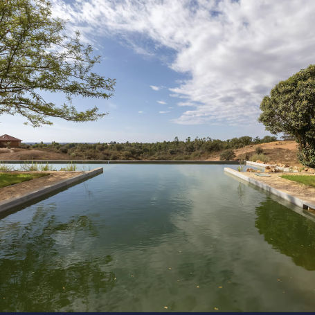 A calm lake reflecting the sky, surrounded by greenery and distant hills.
